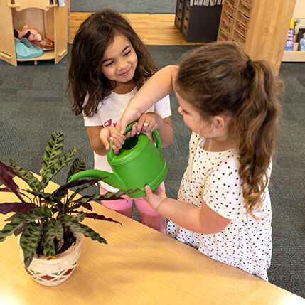 two girls watering a plant at pathways learning academy preschool